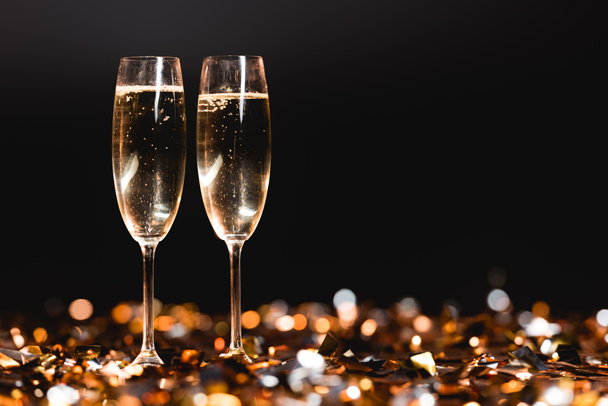 champagne glasses on golden confetti on black for new year celebration - Photo, Image
