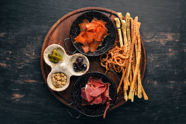 A selection of snacks for beer. Fish, prosciutto, peanuts, olives. On a wooden background. Free copy space. Top view. - Fotó, kép