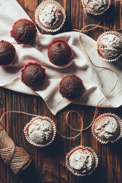 Draufsicht auf leckere gebackene Muffins und Garnspule auf Holztisch in Bäckerei - Foto, Bild