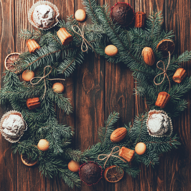 top view of fir wreath with tasty baked cookies and muffins on wooden table, christmas concept - Fotografie, Obrázek
