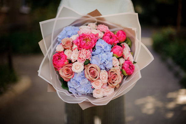 Woman in the white sweather holding in her hands bouquet of tender pink and blue flowers in white transparent paper - Photo, image