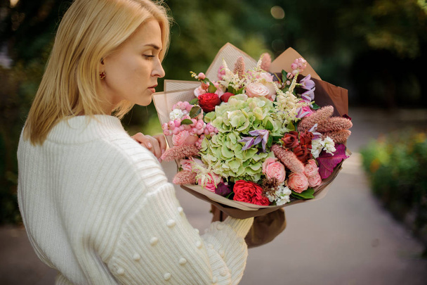 Rear view girl in the white sweather holding in her hands bouquet of tender autumn flowers in brown paper - Fotografie, Obrázek