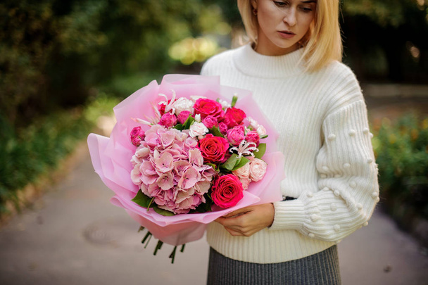 Woman in the white sweather holding in her hands bouquet of tender bright pink flowers in rose color paper - Fotoğraf, Görsel