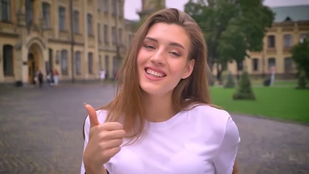 pretty caucasian girl showing like sign while standing on the street and smiling, daytime, city view. - Imágenes, Vídeo