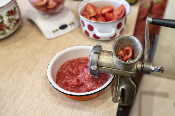Torça tomates em purê de tomate com um velho moedor de mão. Preparação de produtos hortícolas em conserva em casa
 - Foto, Imagem