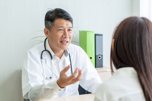 Asian senior doctor and patient are discussing something while sitting at the table - Фото, изображение