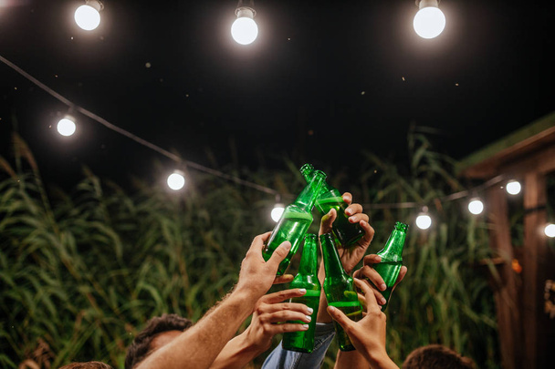 Hands of group of unrecognisable people toasting with beer bottles at outdoor party. - Foto, Imagem