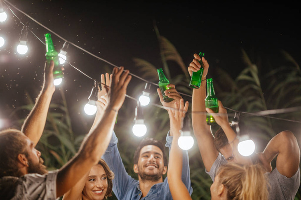 Group of men and women toasting with beer bottles at outdoor party. - Foto, Imagem