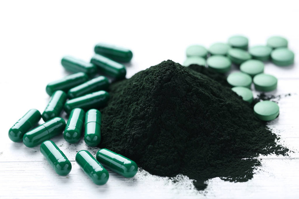 Spirulina powder in heap and tablets on white wood - Photo, Image