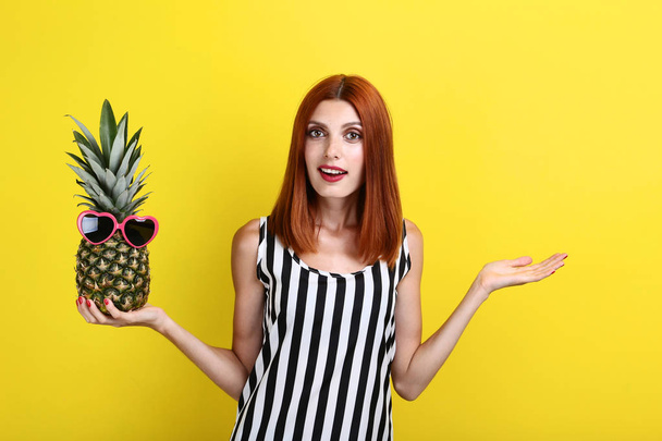 Beautiful redhaired woman with pineapple on yellow background - Фото, зображення