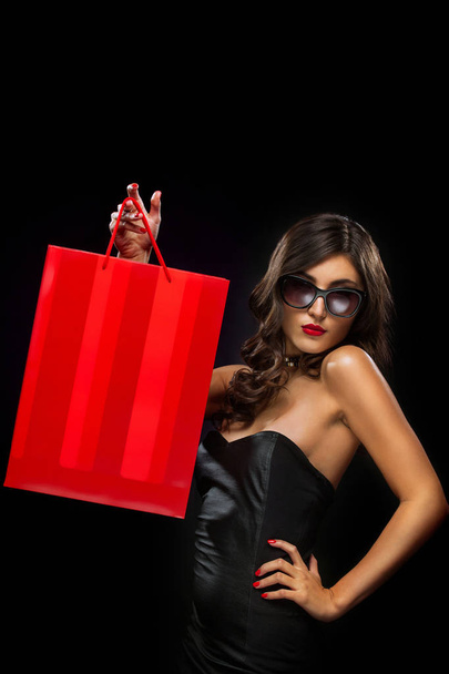 Black friday sale concept. Shopping woman holding red bag isolated on dark background in holiday - Fotografie, Obrázek