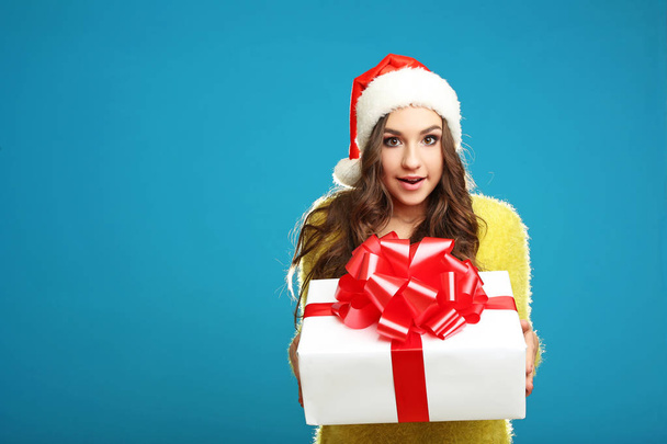 young girl in santa claus hat holding gift box on blue background - Foto, imagen