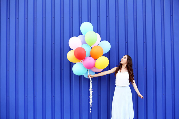 Menina bonito com balões coloridos em pé no fundo azul
 - Foto, Imagem