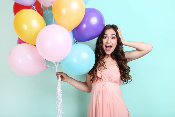 surprised young girl in pink dress with colored balloons standing on mint background - Zdjęcie, obraz