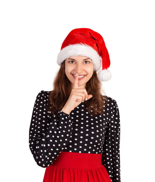 Pleasant woman keeps finger on lips, asks not tell secret information or keep silence. emotional girl in santa claus christmas hat isolated on white background. holiday concept. - Photo, Image