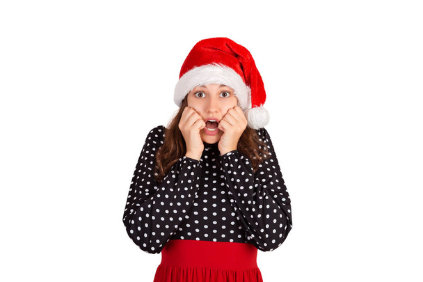 Scared woman looks nervously, biting fingernails and afraid of something. emotional girl in santa claus christmas hat isolated on white background. holiday concept. - Photo, Image