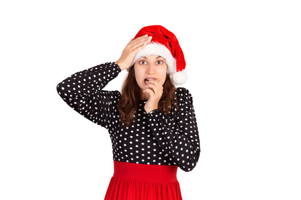 Разочарованная женщина чувствует тревогу и удивляется и кусает ногти в недоумении. эмоциональная девушка в рождественской шляпе Санта Клауса изолирована на белом фоне. Концепция отдыха
. - Фото, изображение