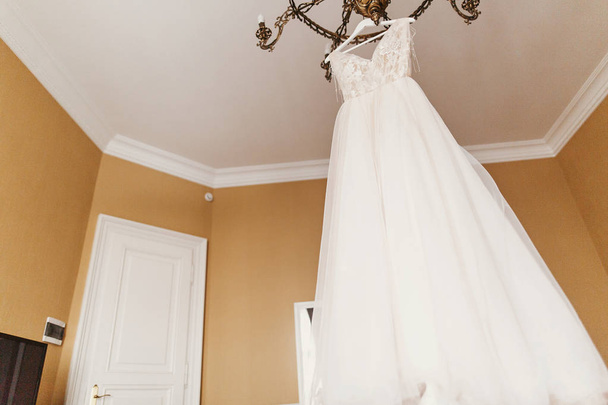 Elegantní svatební šaty. Moderní svatební šaty visí na lustru v pokoji. Prostor pro text. Příslušenství, nevěsta na svatbu. Svatební salon nebo showroom - Fotografie, Obrázek