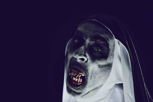 gros plan d'une religieuse maléfique effrayante, avec des dents sanglantes et des yeux effrayants, portant un habit noir et blanc typique, sur un fond noir, avec un peu d'espace vide à gauche
 - Photo, image