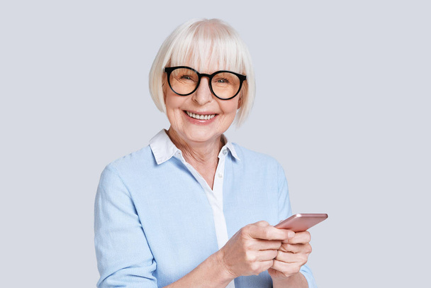 senior caucasian woman in blue shirt holding mobile phone and looking at camera - Foto, Bild