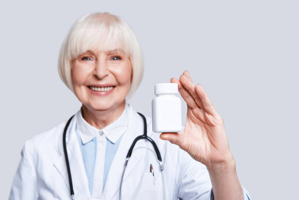smiling senior woman in lab coat holding bottle with medicines  - Foto, Imagen