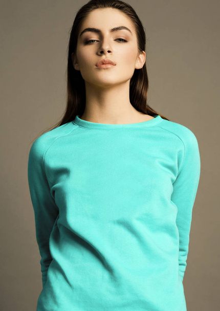 Beautiful fashion model with bright turquoise jumper on grey background - Photo, Image