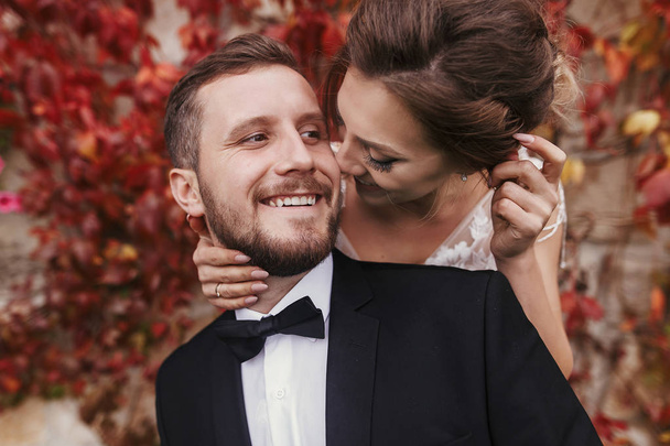 豪華なスタイリッシュな新郎新婦優しく抱き締める、秋の紅葉の壁で笑顔します。幸せな官能的な結婚式のカップルが採用します。新婚のロマンチックな瞬間 - 写真・画像