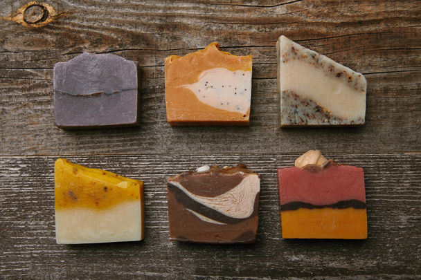 bovenaanzicht van verschillende handgemaakte zeep stukken op rustieke houten tafelblad - Foto, afbeelding