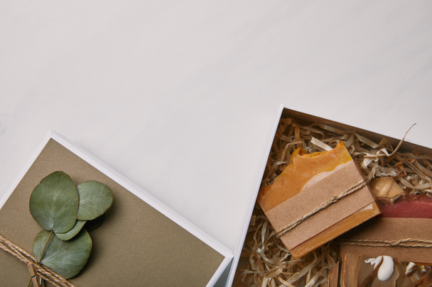 白い大理石の表面に石鹸の中でユーカリの葉で飾られたギフト ボックスのトップ ビュー - 写真・画像