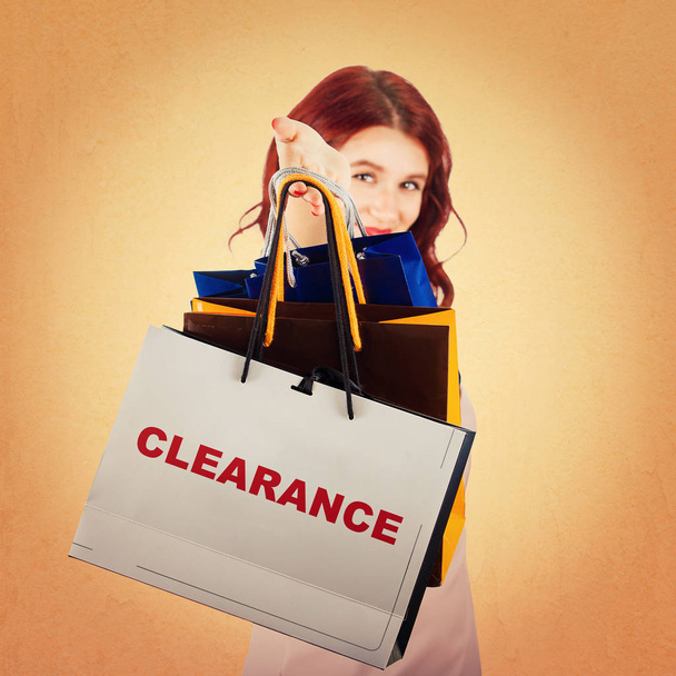 Jonge vrouw hand uitgerekt tot camera houden boodschappentassen als stock clearance voor verkoop seizoen geïsoleerd over kleurrijke achtergrond. - Foto, afbeelding