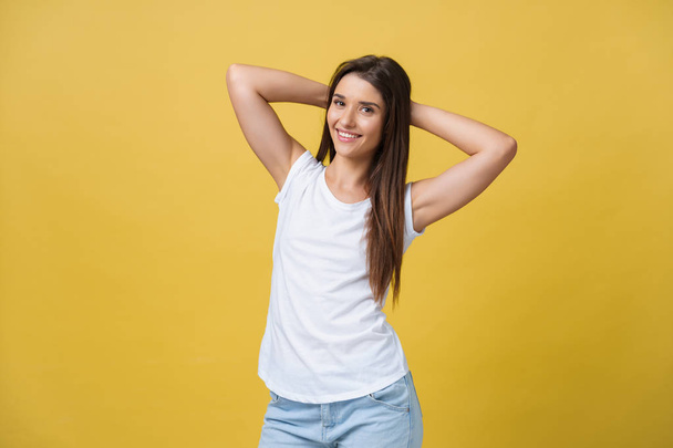 Close-up portrait of cute young woman relaxing with hand behind head. Isolated over yellow background. - Photo, Image