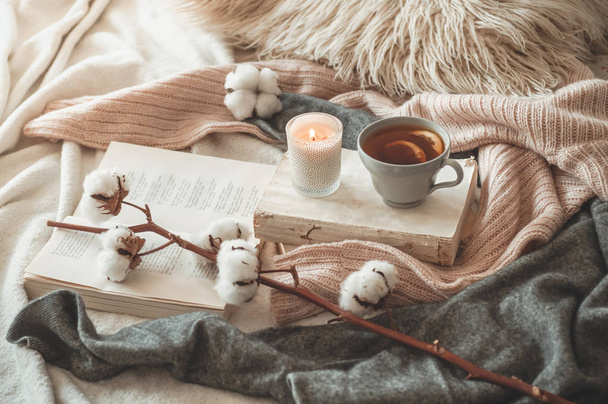 Still life in home interior of living room. Sweaters and cup of tea with a cone  on the books. Read. Cozy autumn winter concept - Photo, Image