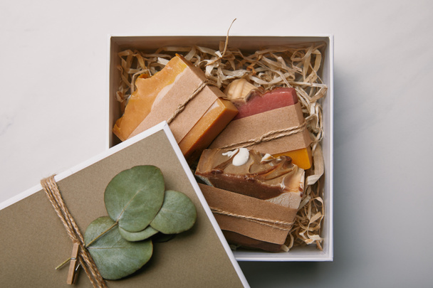 κάτοψη του κουτί διακοσμημένο με φύλλα ευκαλύπτου με σαπούνι μέσα σε λευκή μαρμάρινη επιφάνεια - Φωτογραφία, εικόνα