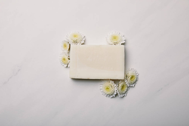 top view of handmade soap piece with daisies on white marble surface - Photo, Image