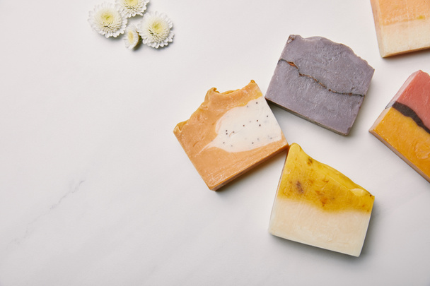 top view of various handmade soap pieces with flowers on white marble surface - Foto, immagini
