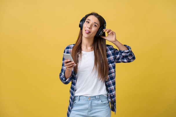 Beautiful young woman in headphones listening to music and dancing on yellow background. - Foto, immagini