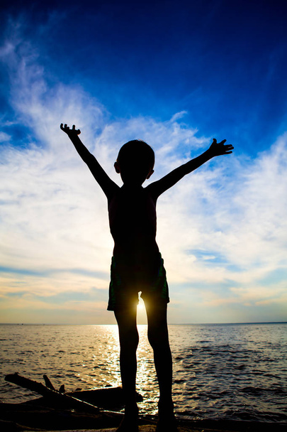 Silhouette enfant heureuse avec les mains dans l'eau sur le coucher du soleil Arrière-plan
 - Photo, image