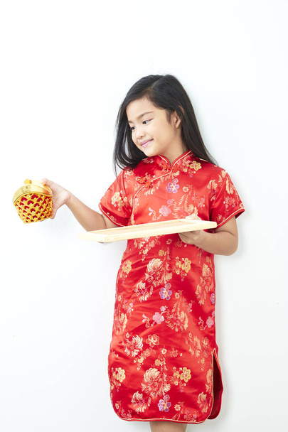 Dívka dítě 8 let v tradiční čínské šaty nový rok 2019 se drží zlatého ingotu stojící na bílé stěně pozadí - Fotografie, Obrázek