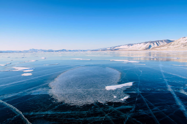 View of beautiful drawings on ice from cracks and bubbles of deep gas on surface of Baikal lake in winter with mountain, Russia - Photo, image