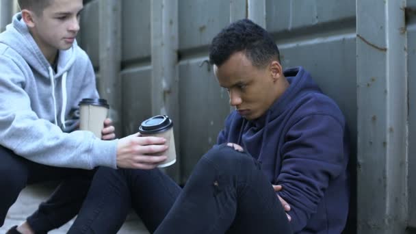 Boy sharing warm coffee with frozen homeless teenager, charity volunteer - Footage, Video