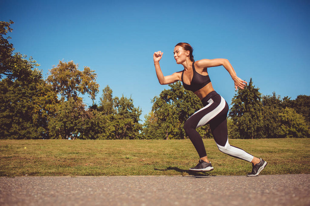 side view of woman in black white leggings and sportive top running in park - Foto, imagen