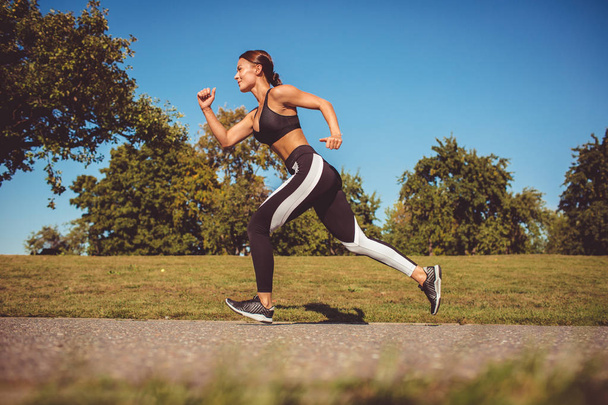 side view of woman in black white leggings and sportive top running in park - Foto, Bild