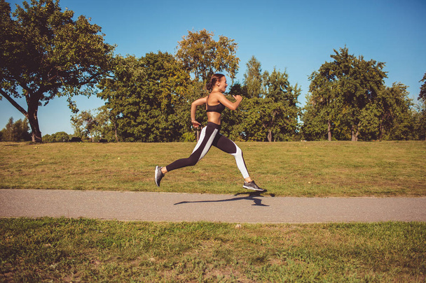 side view of woman in black white leggings and sportive top running in park - Photo, Image