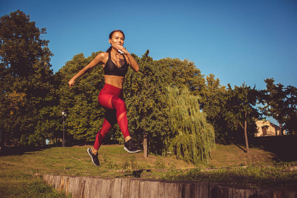 καυκάσιος γυναίκα στο κόκκινο κολάν και sportive κορυφή τρέξιμο και άλματα στο πάρκο - Φωτογραφία, εικόνα