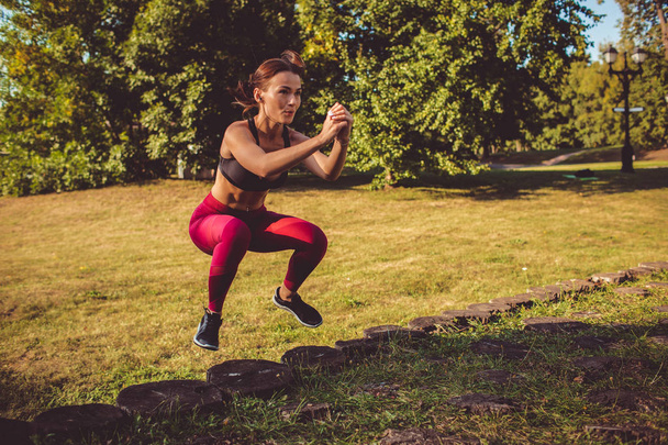 woman in red leggings and sportive top doing squats in park meadow  - Φωτογραφία, εικόνα