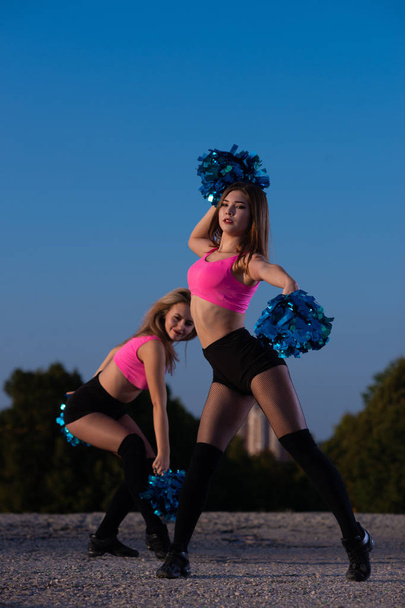 Two girls cheerleaders with pompons dancing outdoors on sky background - Fotó, kép