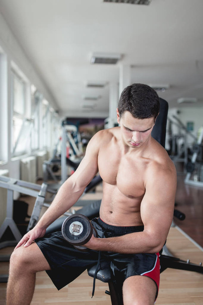 Young attractive adult man exercising and doing weight lifting at fitness gym. Sport training indoors. - Photo, Image