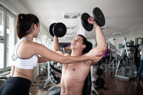 Mladý atraktivní dospělý muž a žena cvičení a dělat Vzpírání na fitness tělocvičně. Sportovní trénink uvnitř. - Fotografie, Obrázek