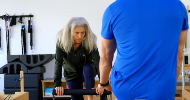 Trainer assisting senior women in performing yoga at yoga center 4k - Materiał filmowy, wideo