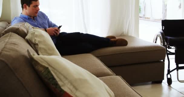 Disabled man using mobile phone on sofa 4k - Πλάνα, βίντεο